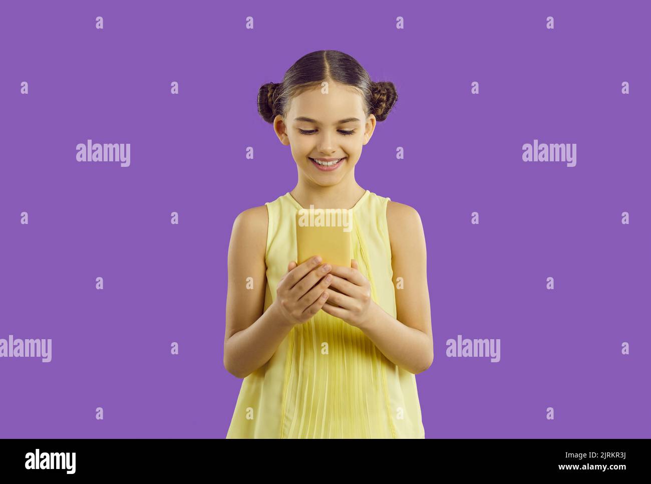 Lächelnd niedlich liebenswert präteen Mädchen genießt mit modernen Smartphone isoliert auf lila Hintergrund. Stockfoto