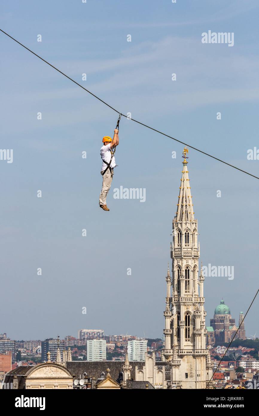 Person, die an einem Seil vor einem Blick auf den Turm des Rathauses von Brüssel hängt Stockfoto