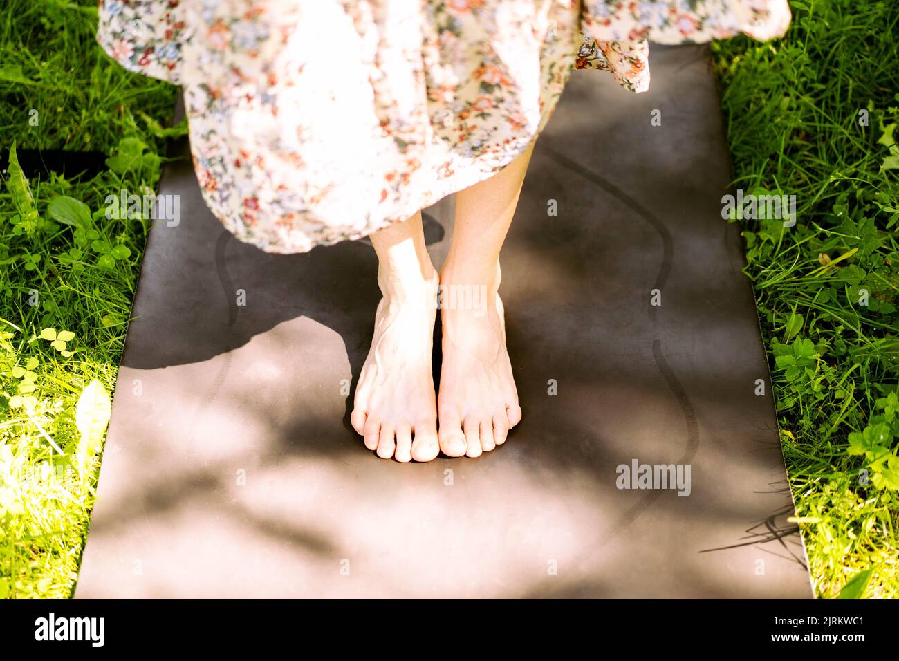 Die Füße eines jungen Mädchens auf einer schwarzen Yogamatte im Sommer inmitten des grünen Grases im Park. Speicherplatz kopieren. Ein großartiger Hintergrund für deine Werbeanzeigen. Ökologisches Konzept. Stockfoto