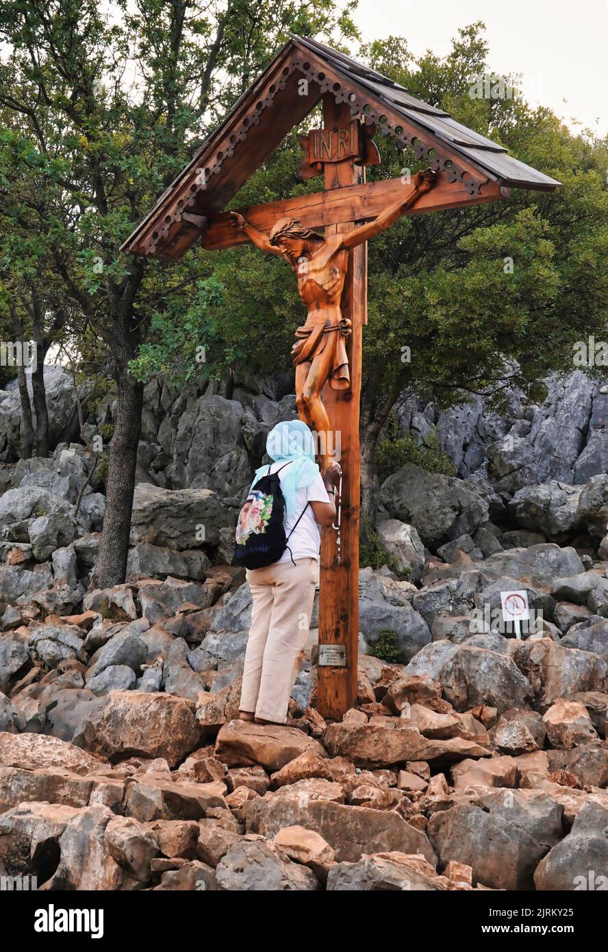 Eine Pilgerin betet vor dem hölzernen Kruzifix, das sich auf dem Podbrdo (Erscheinungsberg) in der Nähe der Statue der seligen Jungfrau Maria (Medjugorje) befindet. Stockfoto