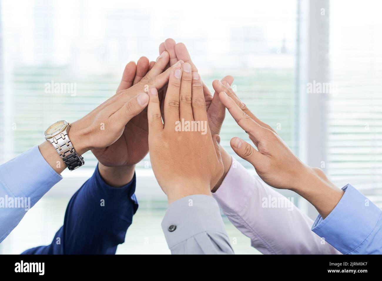 Nahaufnahme von nicht erkennbaren Angestellten mit weißen Kragen, die ihre Hände zusammenfügen und gleichzeitig Einheit zeigen Stockfoto