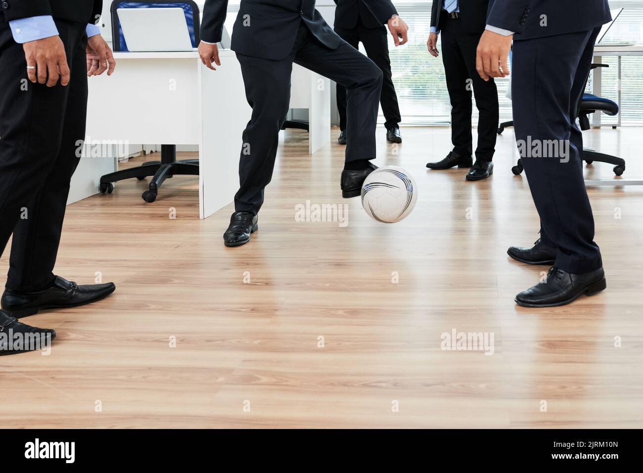 Eine Gruppe von Büromitarbeitern, die Fußball spielen, während sie eine kurze Pause von der Arbeit machen, die Inneneinrichtung des Großraumbüros im Hintergrund Stockfoto