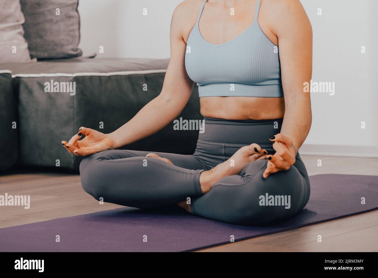 Nahaufnahme Hände einer Frau, die Yoga-Lotuspose macht und in ihrem Zuhause im Wohnzimmer meditiert - Körper beruhigen Lebensstress Entspannen Sie sich in einer Lotuspose Stockfoto