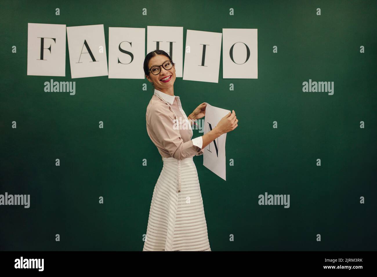 Designerin, die neben der Wand steht und Modewort-Alphabete klebt. Junge Frau hält Alphabet, um an die Studiowand zu kleben. Stockfoto