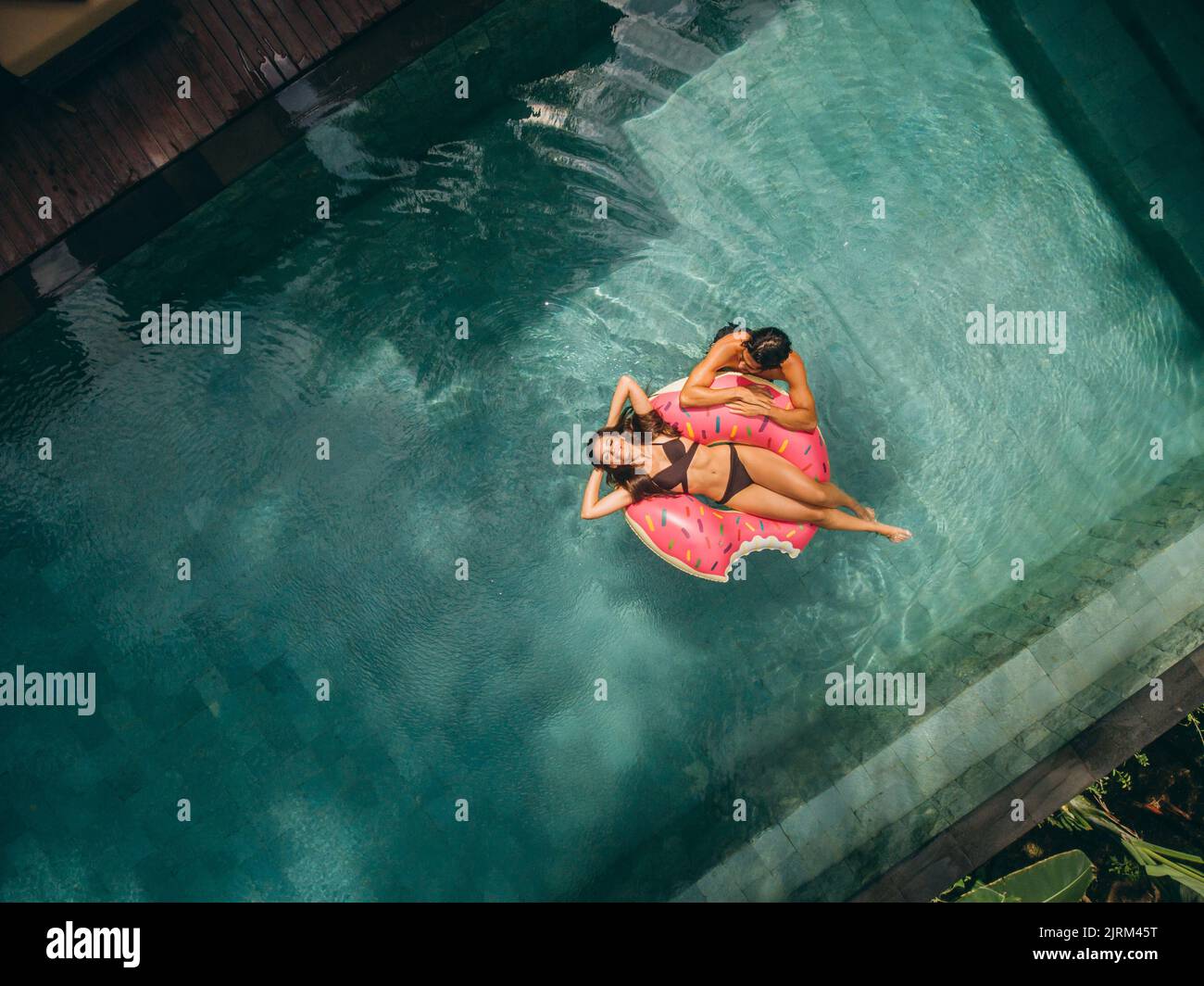 Luftaufnahme einer jungen Frau und einer Frau, die sich auf einem aufblasbaren Ring im Pool des Resorts entspannen. Pärchen genießen ihren Urlaub in einem Luxusresort. Stockfoto