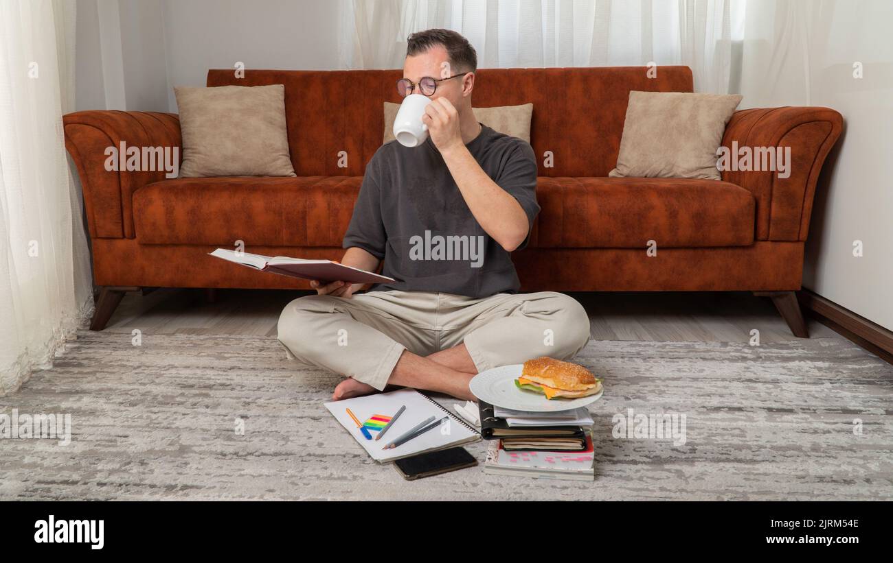 Der Schüler lernt Unterricht und bereitet sich auf die Prüfung vor, trinkt Kaffee, während er ein Buch liest Stockfoto