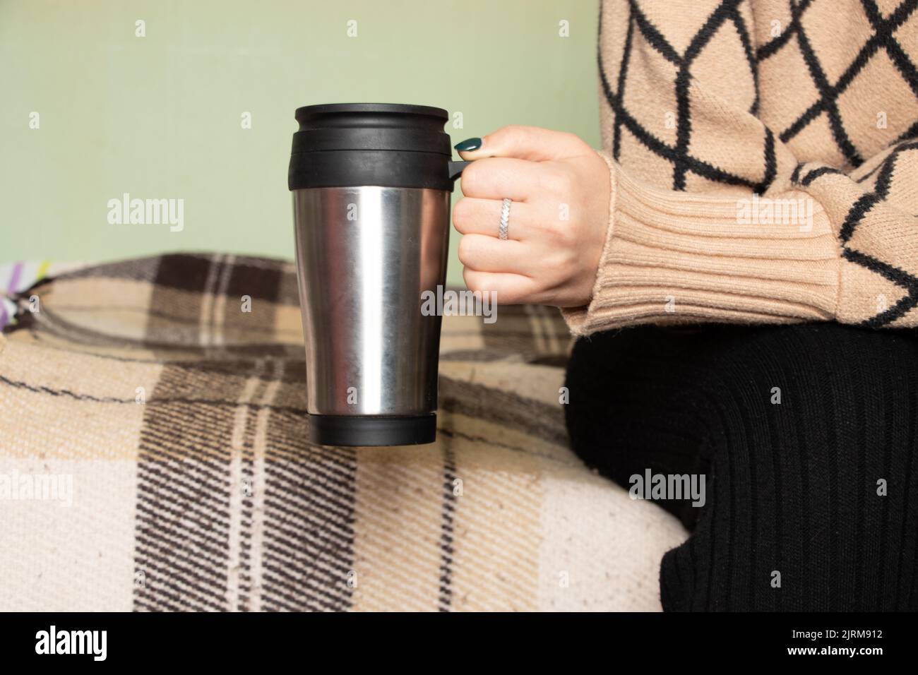 Mädchen hält zu Hause einen grauen Becher in der Hand, trinkt Kaffee, einen freien Tag, eine Tasse in der Hand des Mädchens Stockfoto
