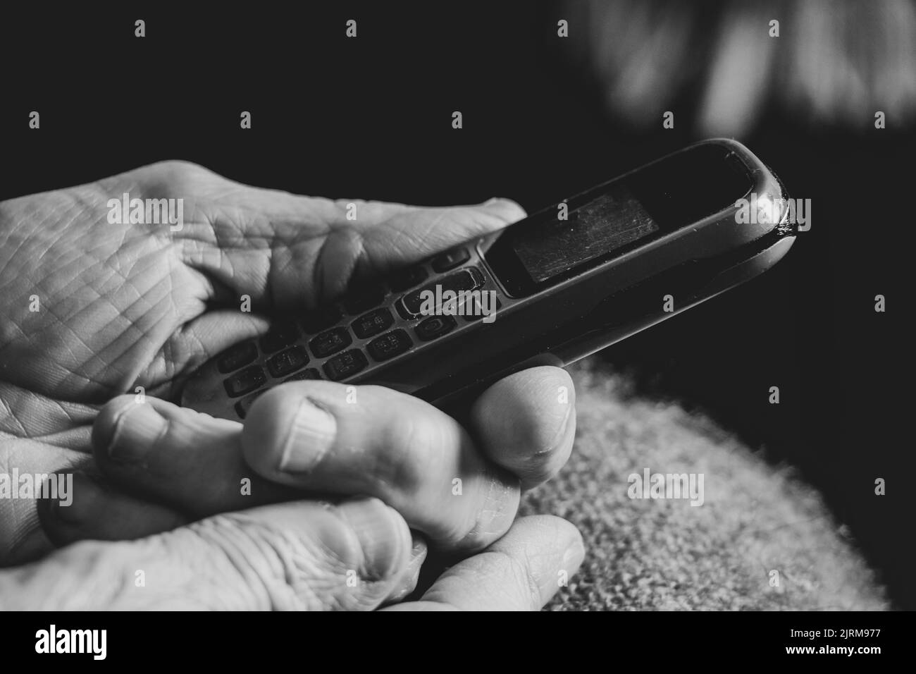 Die Hände der alten Frau halten das Telefon zu Hause, die Rentnerin mit dem Telefon Stockfoto