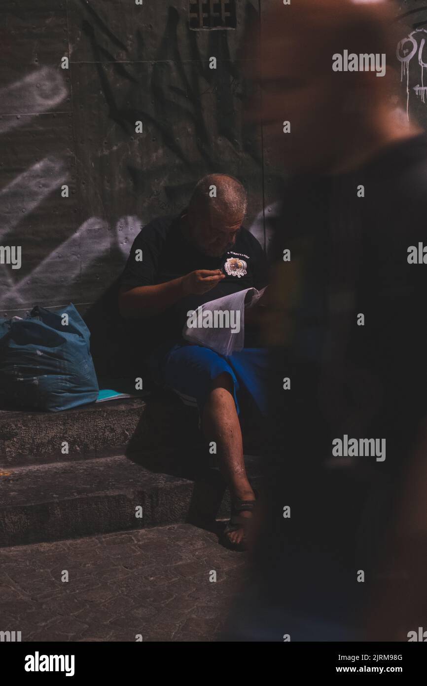 Neapel, Italien - 26. Juli 2022: Porträt eines alten Mannes, der ein Buch über die Treppe liest. Stockfoto