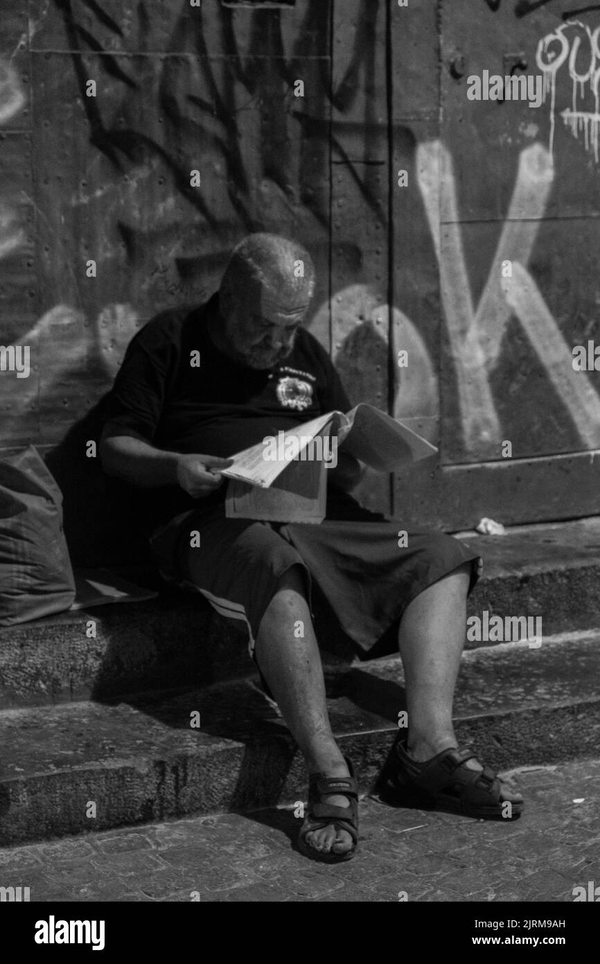 Neapel, Italien - 26. Juli 2022: Porträt eines alten Mannes, der ein Buch über die Treppe liest. Stockfoto