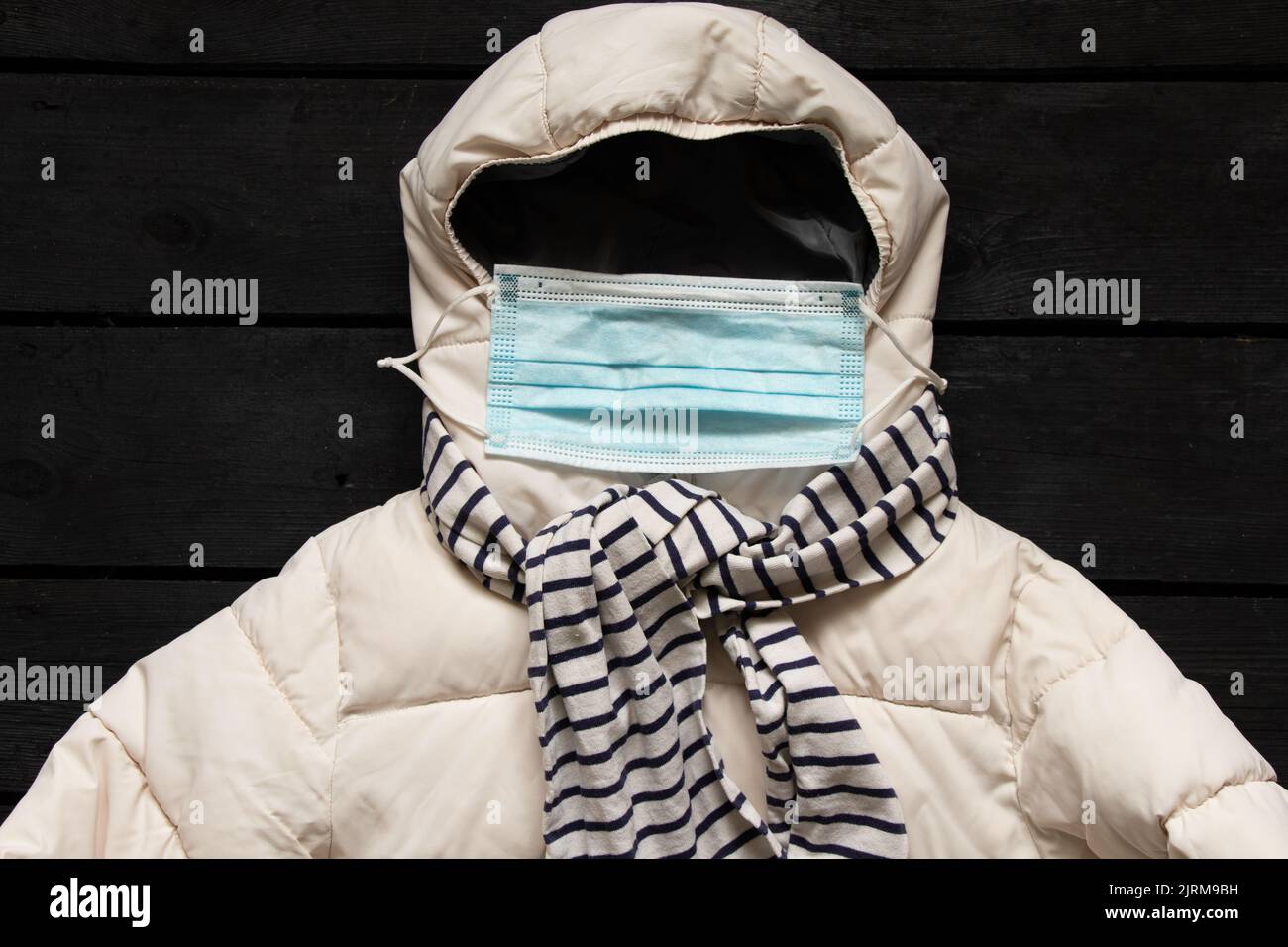 Weißer Winterjackentuch und medizinische Maske auf schwarzem Holztisch, Winterkleidung auf dem Tisch, flaches Lay, Quarantäne- und medizinische Maske und Wintertuch Stockfoto