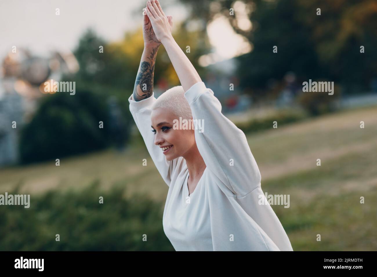 Porträt einer jungen, lächelnden, tausendjährigen europäischen Kurzhaarigen, die im Park Yoga macht. Schöne glücklich blonde Mädchen im Freien. Stockfoto