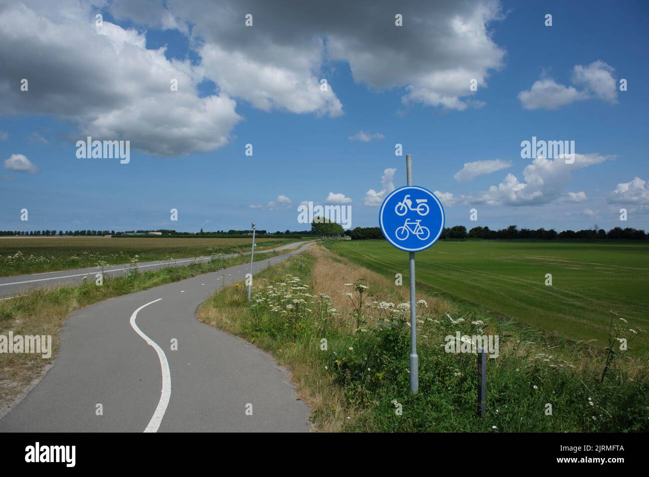Schlängelnde, düstere Rad- und Wanderwege in einer ländlichen Gegend. Es ist ein leicht bewölktes Wetter zu Beginn des Sommers in den Niederlanden. Stockfoto