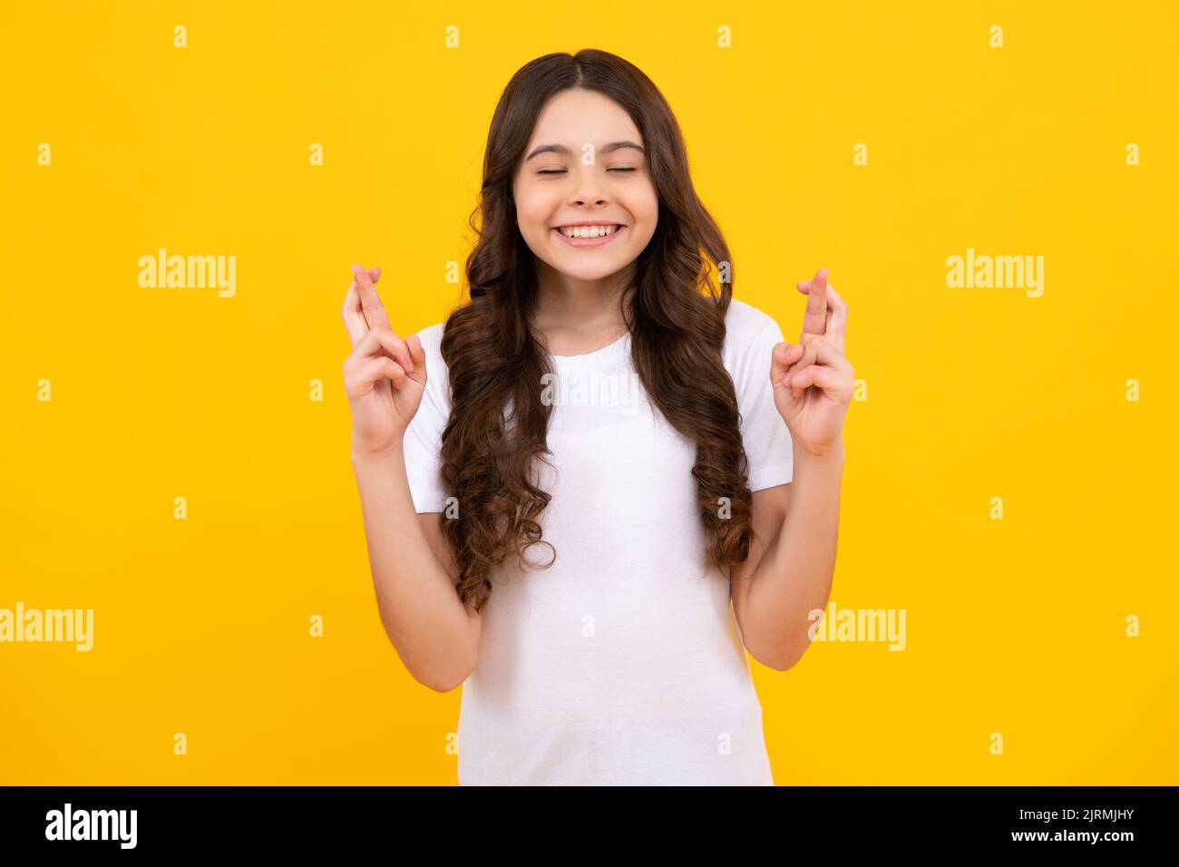Teenager Kind Mädchen, die ihre Finger kreuzt und viel Glück wünscht, isoliert auf gelbem Studiohintergrund mit Kopierraum. Stockfoto