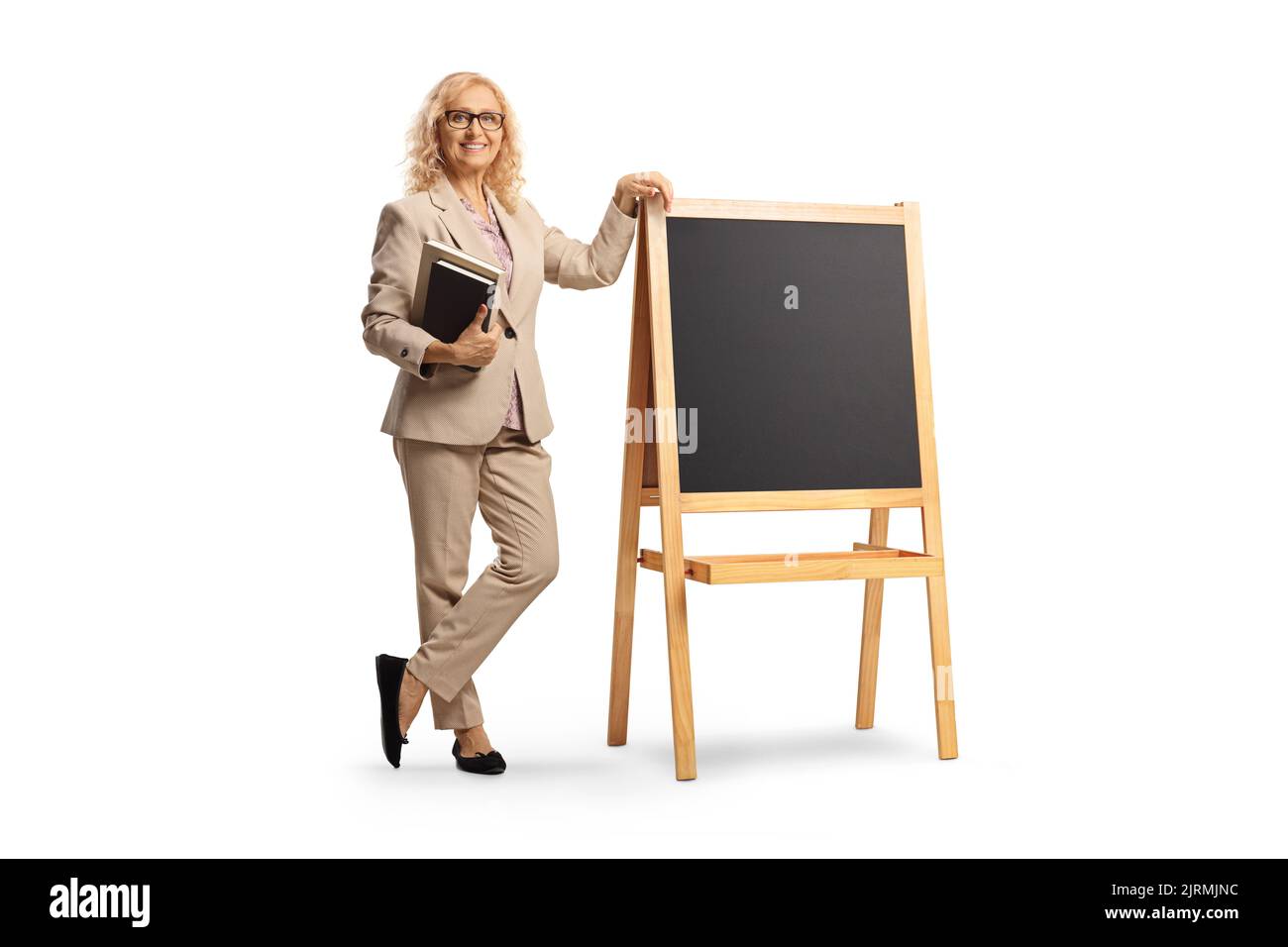 In voller Länge Porträt einer Lehrerin, die Bücher hält und neben einer Tafel steht, isoliert auf weißem Hintergrund Stockfoto
