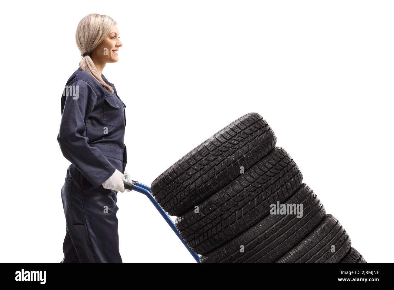 Weibliche Automechanikerin, die auf einem Hand-Truck auf weißem Hintergrund die Reifen läuft und schiebt Stockfoto