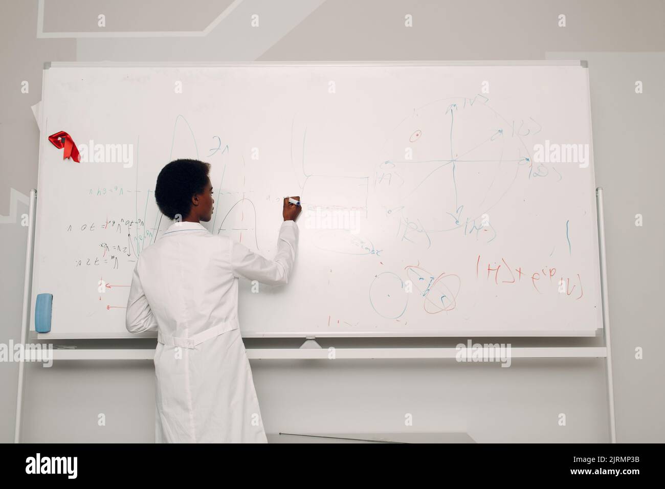 Afroamerikanische Mathematiklehrerin schreibt auf Tafel mit Marker. Stockfoto
