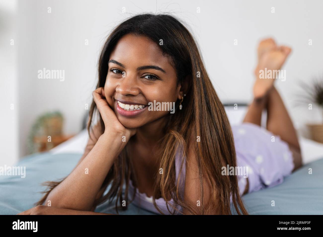 Junge lateinerin lächelt der Kamera zu, während sie zu Hause auf dem Bett liegt Stockfoto
