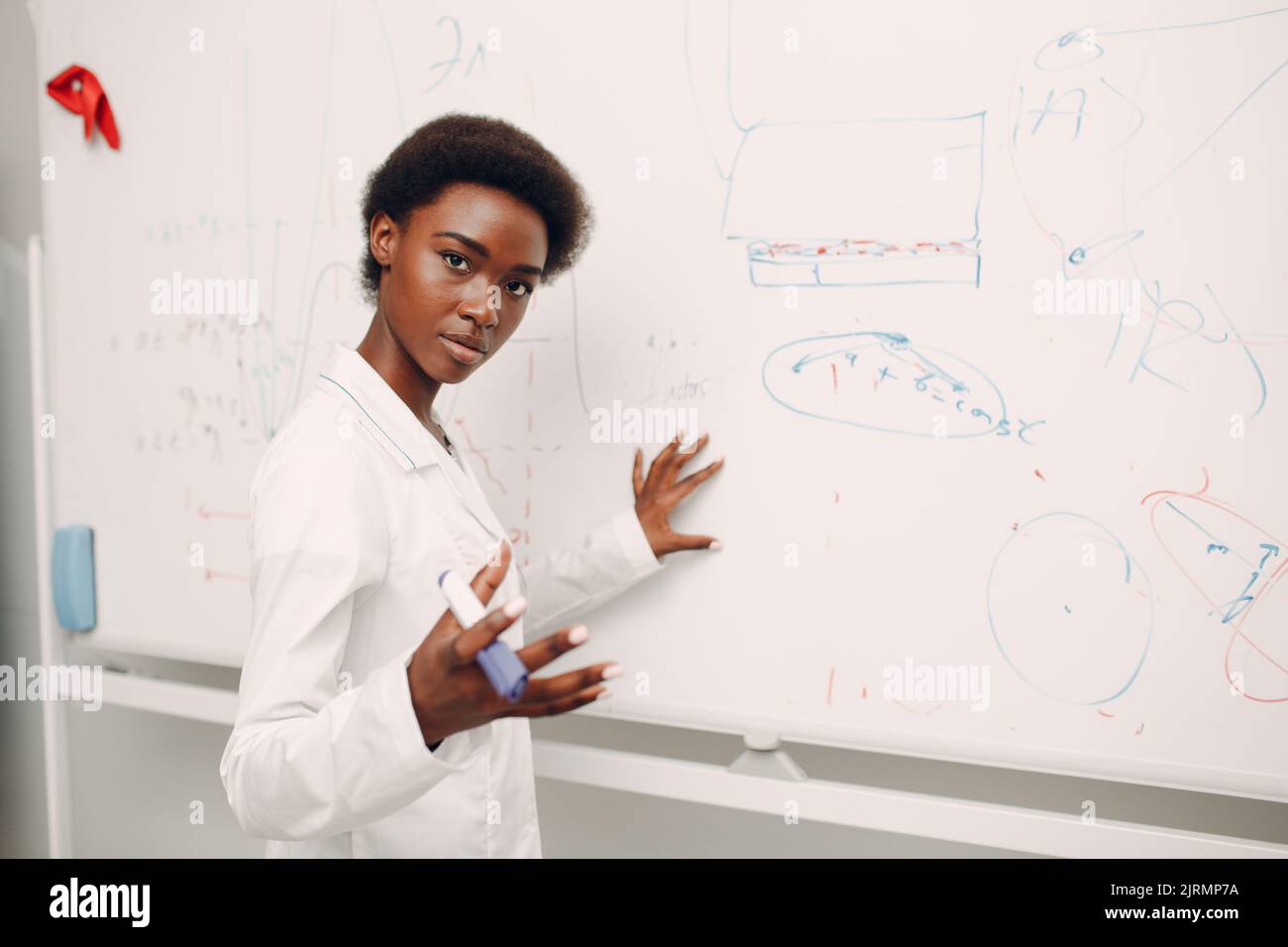 Afroamerikanische Mathematiklehrerin schreibt auf schwarzes Brett mit Marker. Stockfoto