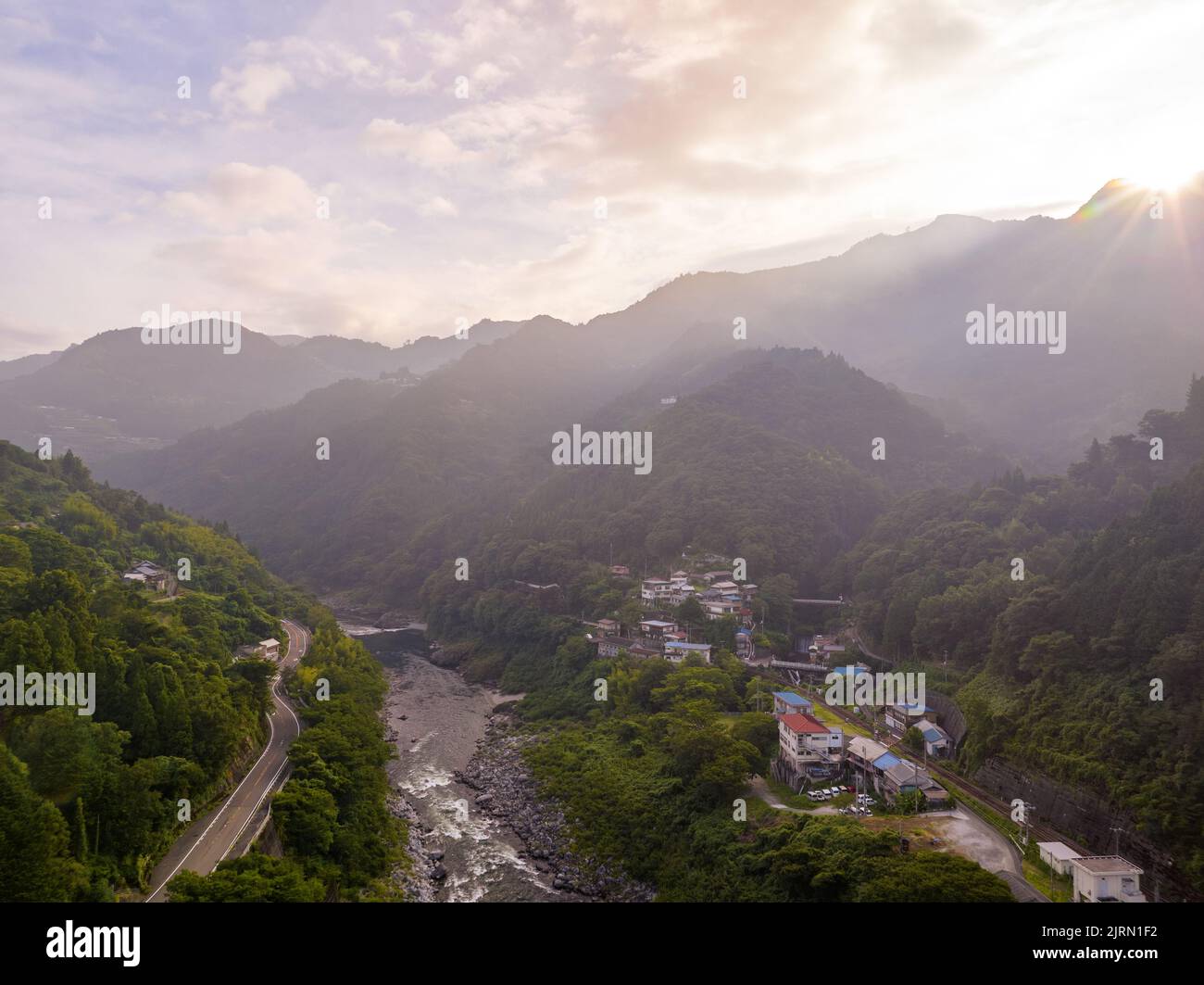 Am frühen Morgen strahlen die Sonnenstrahlen über den Bergen in eine kleine Stadt am Fluss im Tal Stockfoto