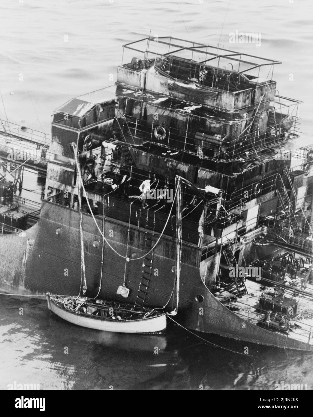 Ein Vintage-Foto aus dem Jahr 1942, das zeigt, dass ein Handelsschiff nach der Torpedoroführung eines deutschen U-Bootes bei der Überquerung des Atlantischen Ozeans während des Zweiten Weltkriegs untergeht. Die Besatzung hat ein Rettungsboot abgesenkt und versucht, das Schiff zu verlassen Stockfoto