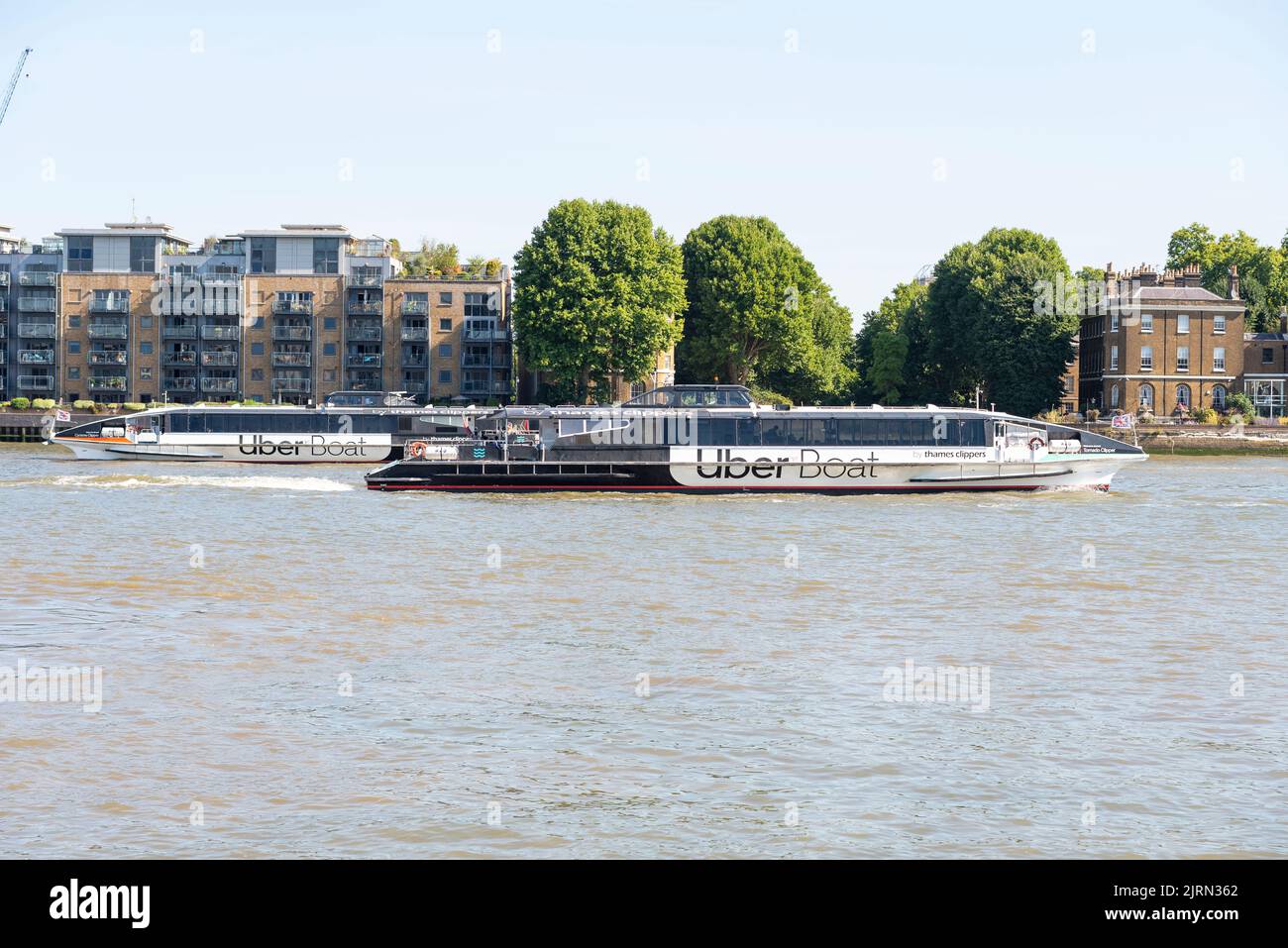 Uber Boat by Thames Clippers River Bus Service-Schiffe, die an den Apartments am Flussufer der Themse vorbeifahren, London, Großbritannien. Flussverkehrssystem Stockfoto