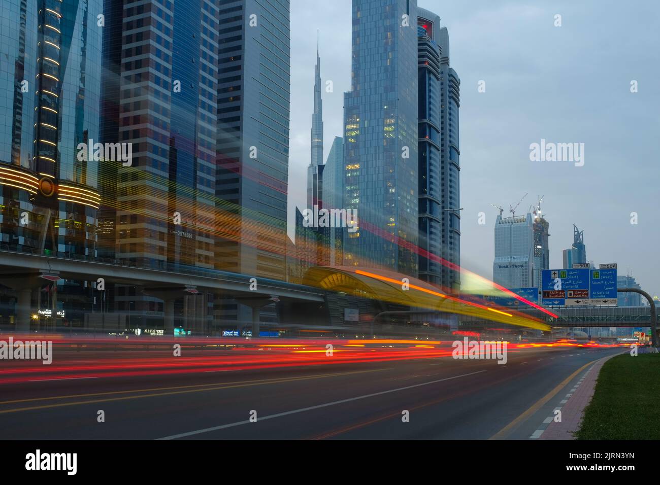 Gebäude und rasende Autos entlang der Sheikh Zayed Road, der längsten Autobahn in Dubai und den Vereinigten Arabischen Emiraten. Stadtbild im Freien bei Dämmerung. Stockfoto
