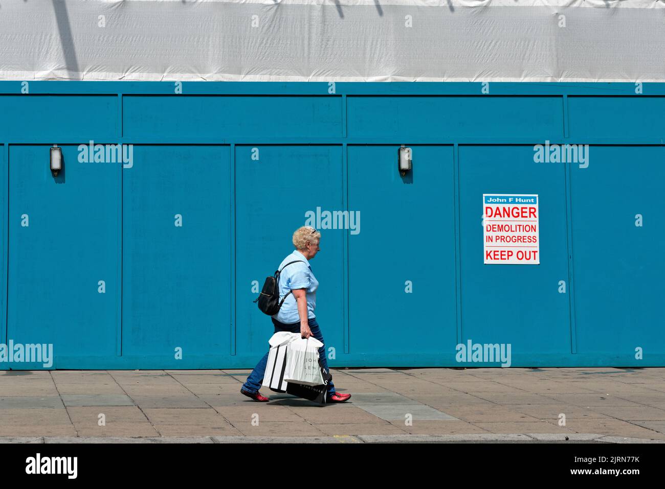 Eine alleinstehende ältere Frau, die an einem blauen Gebäude vorbeikommt und ein abstraktes Bild auf der Londoner Oxford Street England erstellt Stockfoto