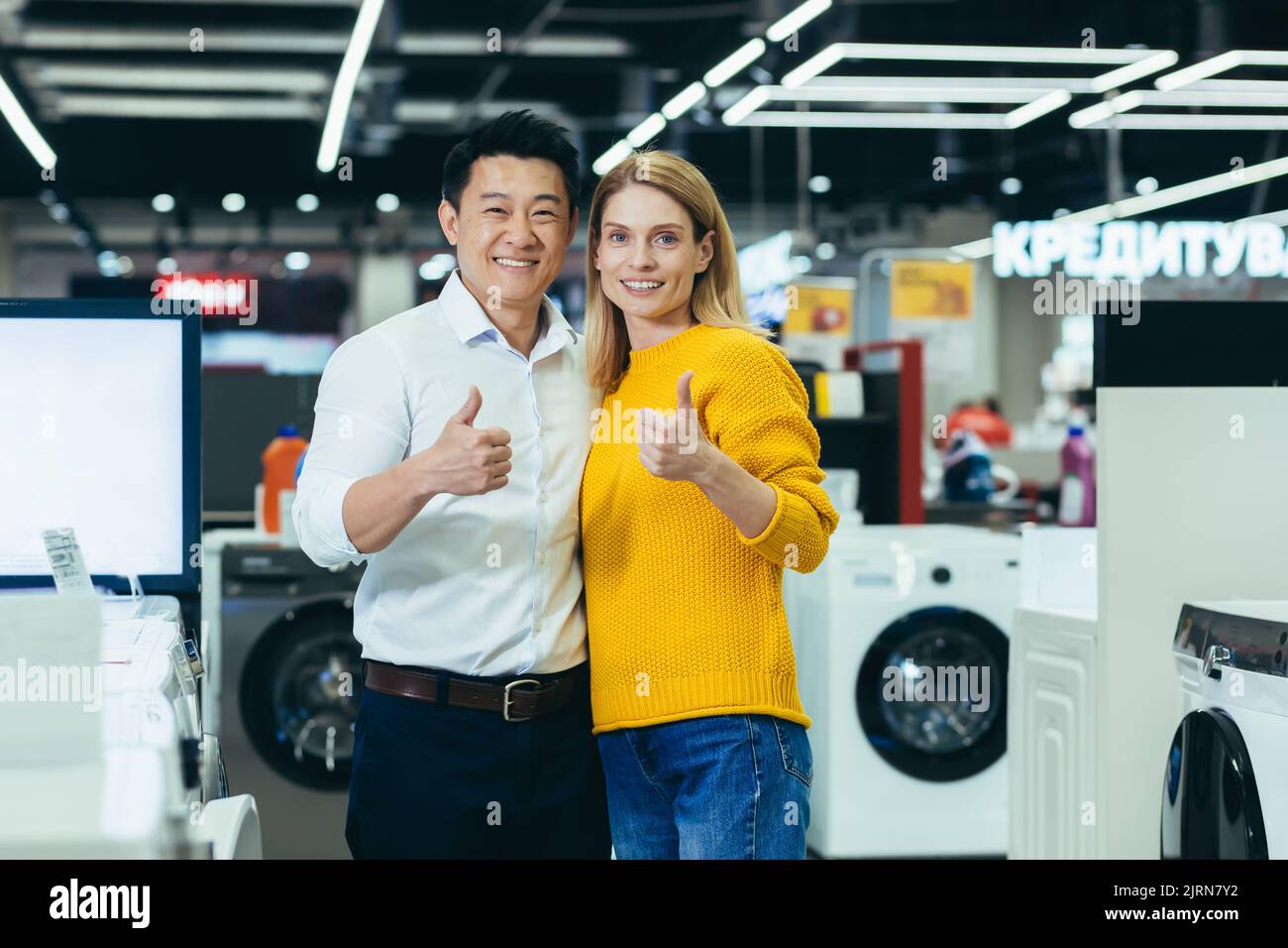 Zufrieden verschiedene paar Käufer Asiatische Mann und Frau lächeln und schauen auf die Kamera, zufrieden und positiv und empfehlen Geschäft halten Daumen hoch, Käufer im Elektronikgeschäft Stockfoto