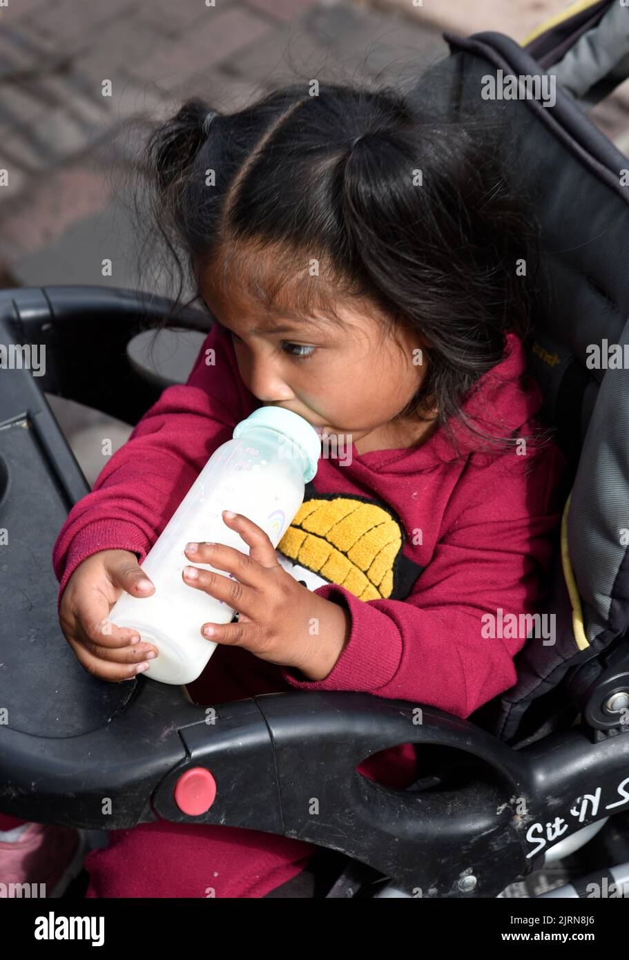 Ein indianisches Kind in einer Babykutsche trinkt beim jährlichen Santa Fe Indian Market Kunstfestival in Santa Fe, New Mexico, aus einer Babyflasche. Stockfoto