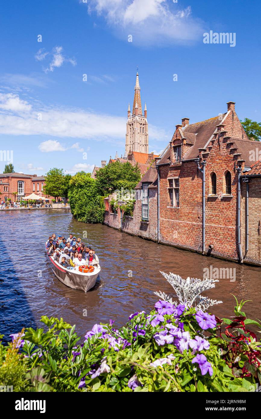 Der Turm der Kirche unserer Lieben Frau (Onze-Lieve-Vrouwekerk) mit Blick auf Touristen genießen eine Bootsfahrt und alte Häuser am Kanal in Brügge, Belgien Stockfoto