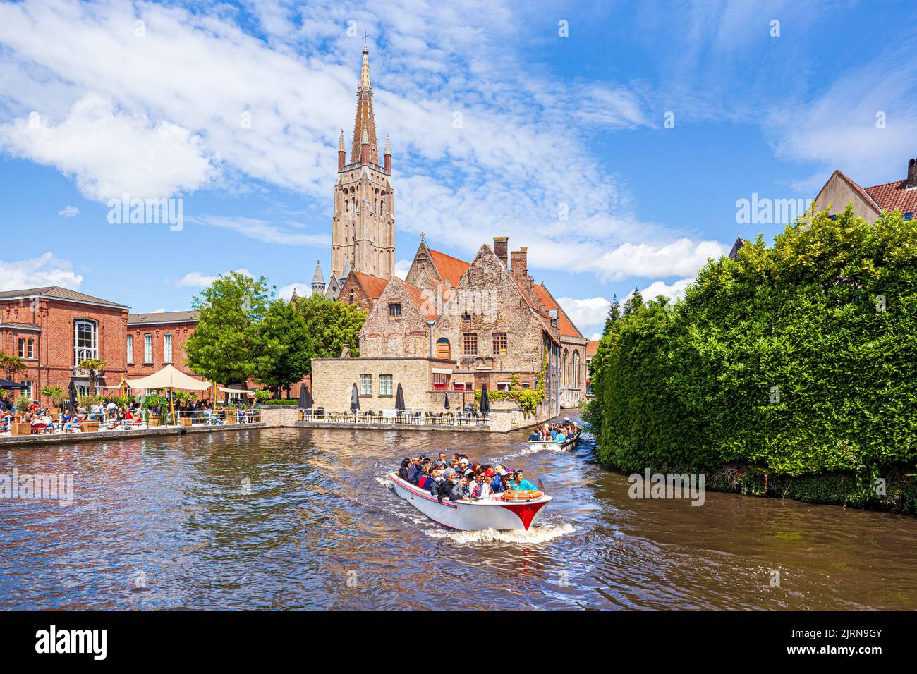 Der Turm der Kirche unserer Lieben Frau (Onze-Lieve-Vrouwekerk) mit Blick auf St. Johns Hospital (Sint-Janshospitaal) und Touristen genießen eine Bootsfahrt auf dem Stockfoto