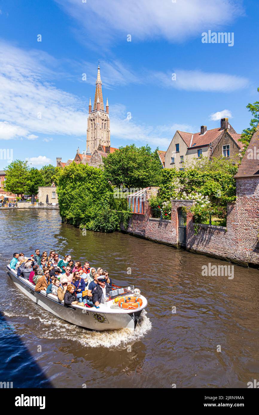 Der Turm der Kirche unserer Lieben Frau (Onze-Lieve-Vrouwekerk) mit Blick auf Touristen genießen eine Bootsfahrt und alte Häuser am Kanal in Brügge, Belgien Stockfoto