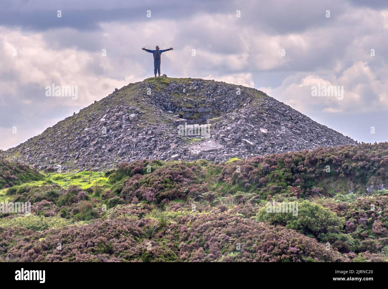 Eine Silhouette eines Mannes, der mit ausgestreckten Armen auf einem Berg steht. Stockfoto