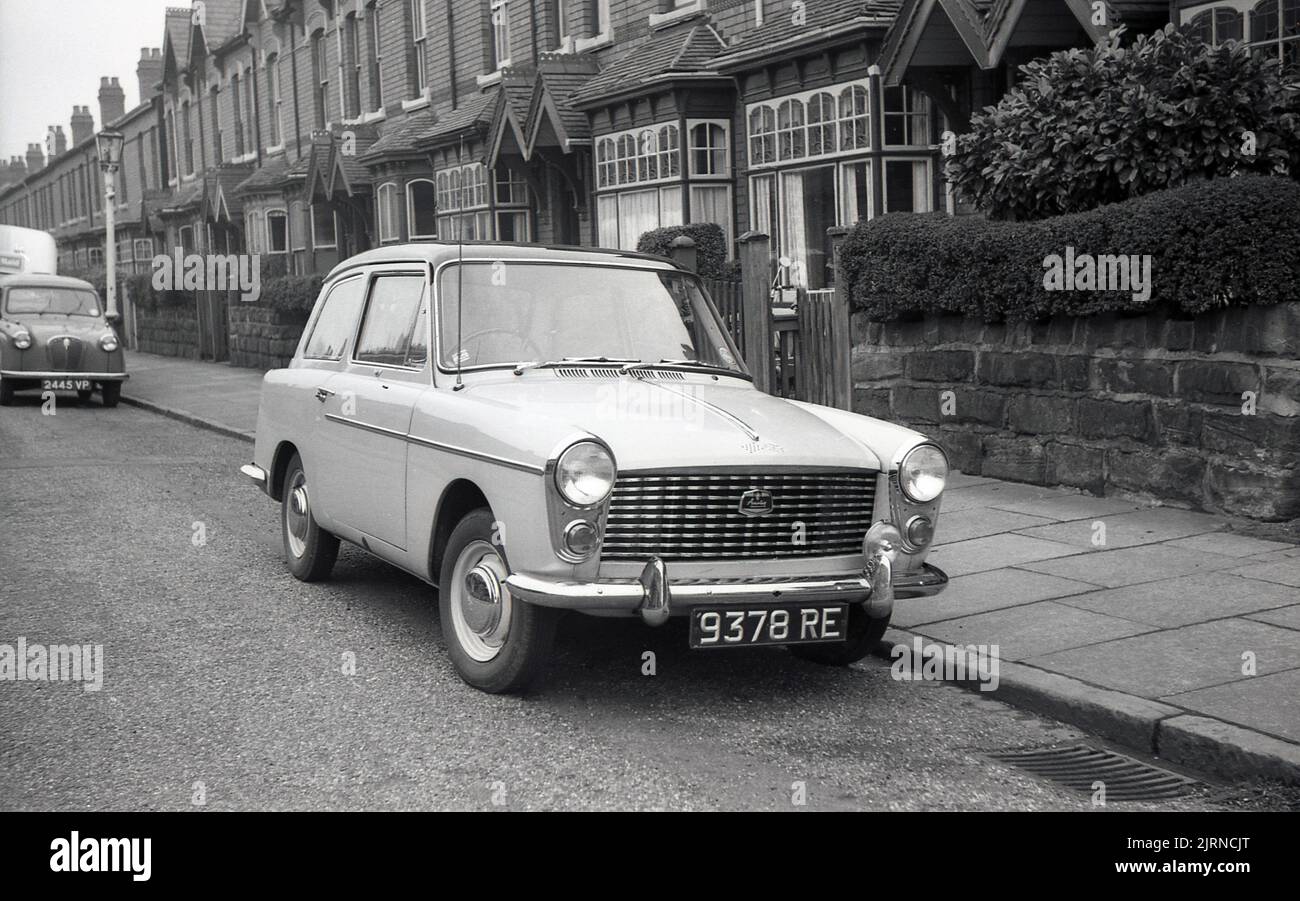 1958, historisch, in einer Vorstadtstraße aus Reihenhäusern, ein Austin A40 Farina Auto der Zeit, geparkt neben dem Bürgersteig, England, Großbritannien. Es handelt sich um ein modernes kleines Auto mit einer markanten „zwei-Kasten“-Form und Kopffreiheit auf dem Rücksitz, das von dem berühmten italienischen Automobildesigner Battista Farina entworfen wurde, der für seine Arbeit mit Ferrari und dem Alfa Romeo Spider berühmt ist. Stockfoto