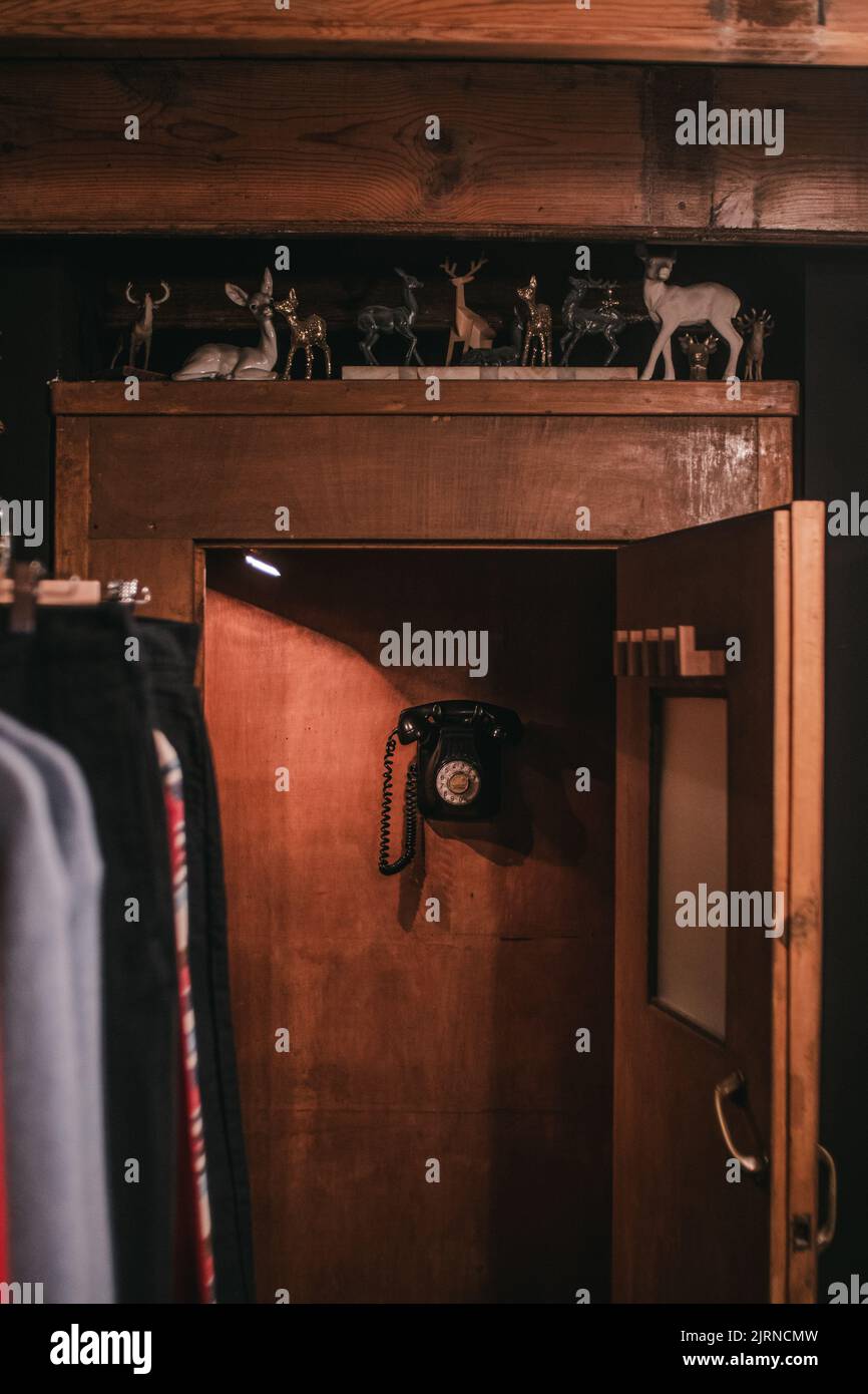 Eine vertikale Aufnahme eines Raumes mit Kleidung, einer Holztür mit Hirschstatuen und einem schwarzen Hängetelefon Stockfoto
