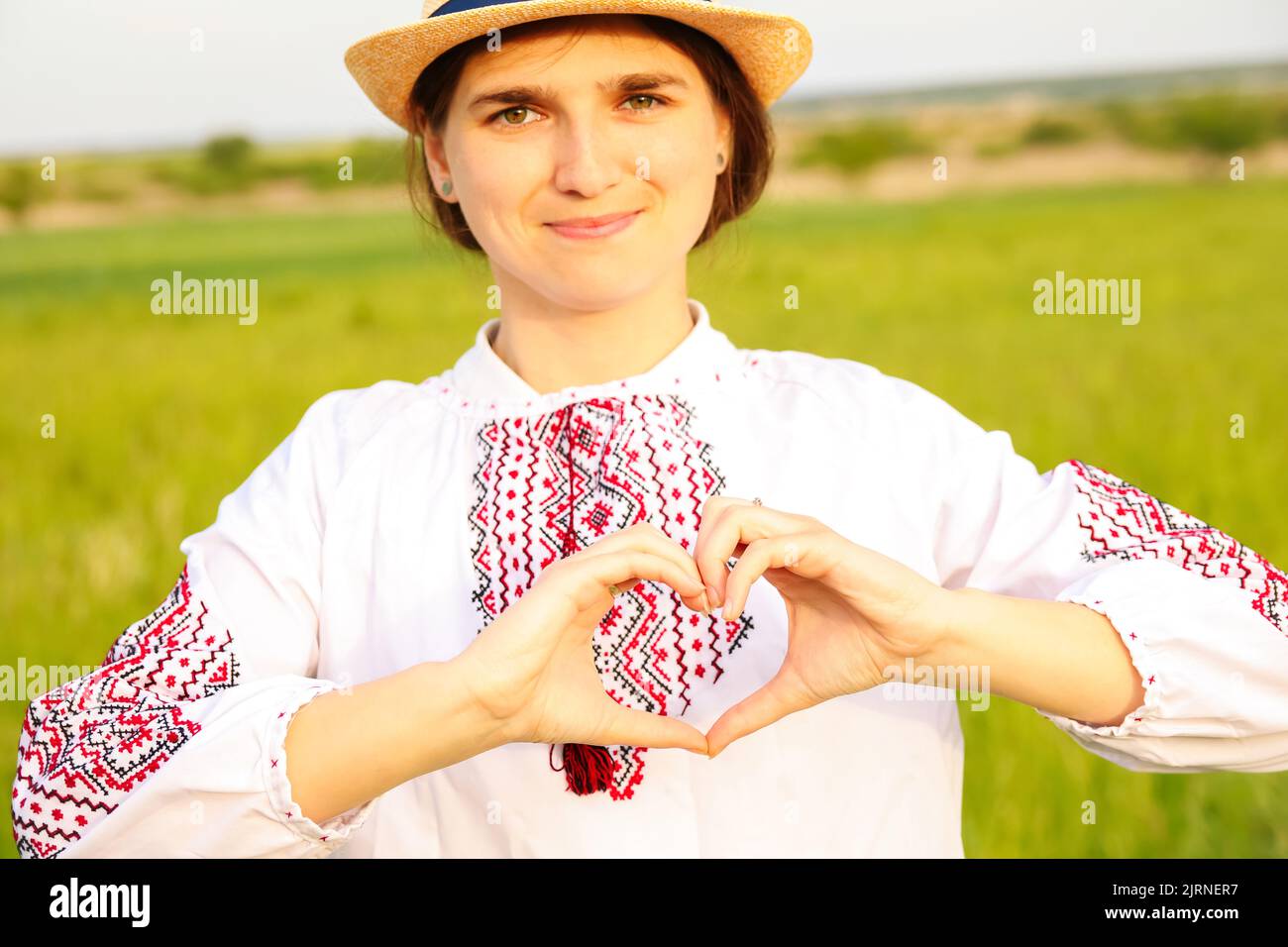 Unschärfe junge ukrainische Frau Porträt. Wiese Natur Hintergrund. Zeichen zeigen Liebe Ukraine. Lächelndes ukrainisches Mädchen zeigt Geste Liebe. Nicht fokussiert Stockfoto