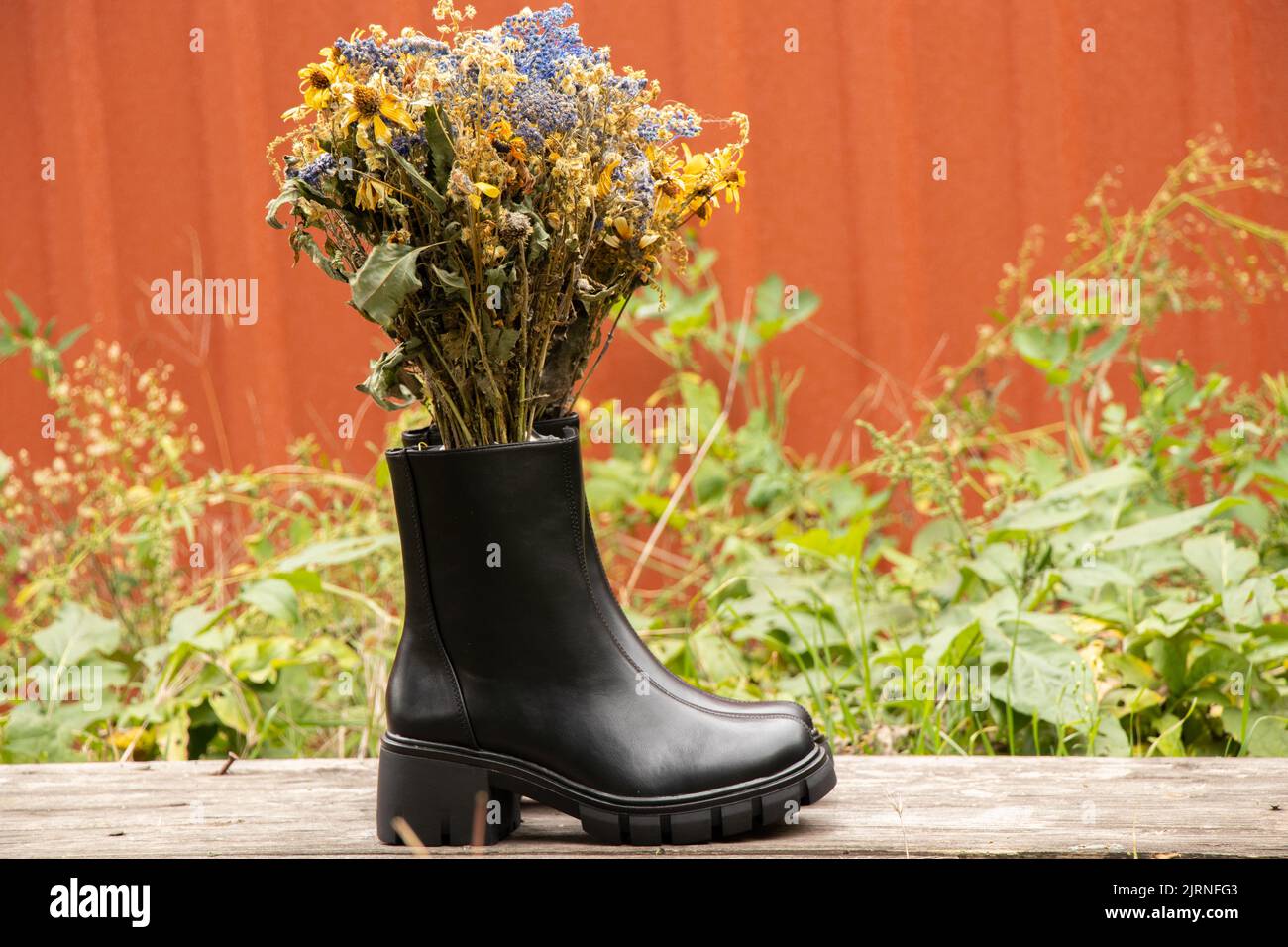 Hohe schwarze Damenstiefel mit dicken Sohlen stehen auf einem Holztisch mit einem Strauß wilder Blumen im Inneren des Schuhs, Winterschuhe für Frauen, Fuß Stockfoto