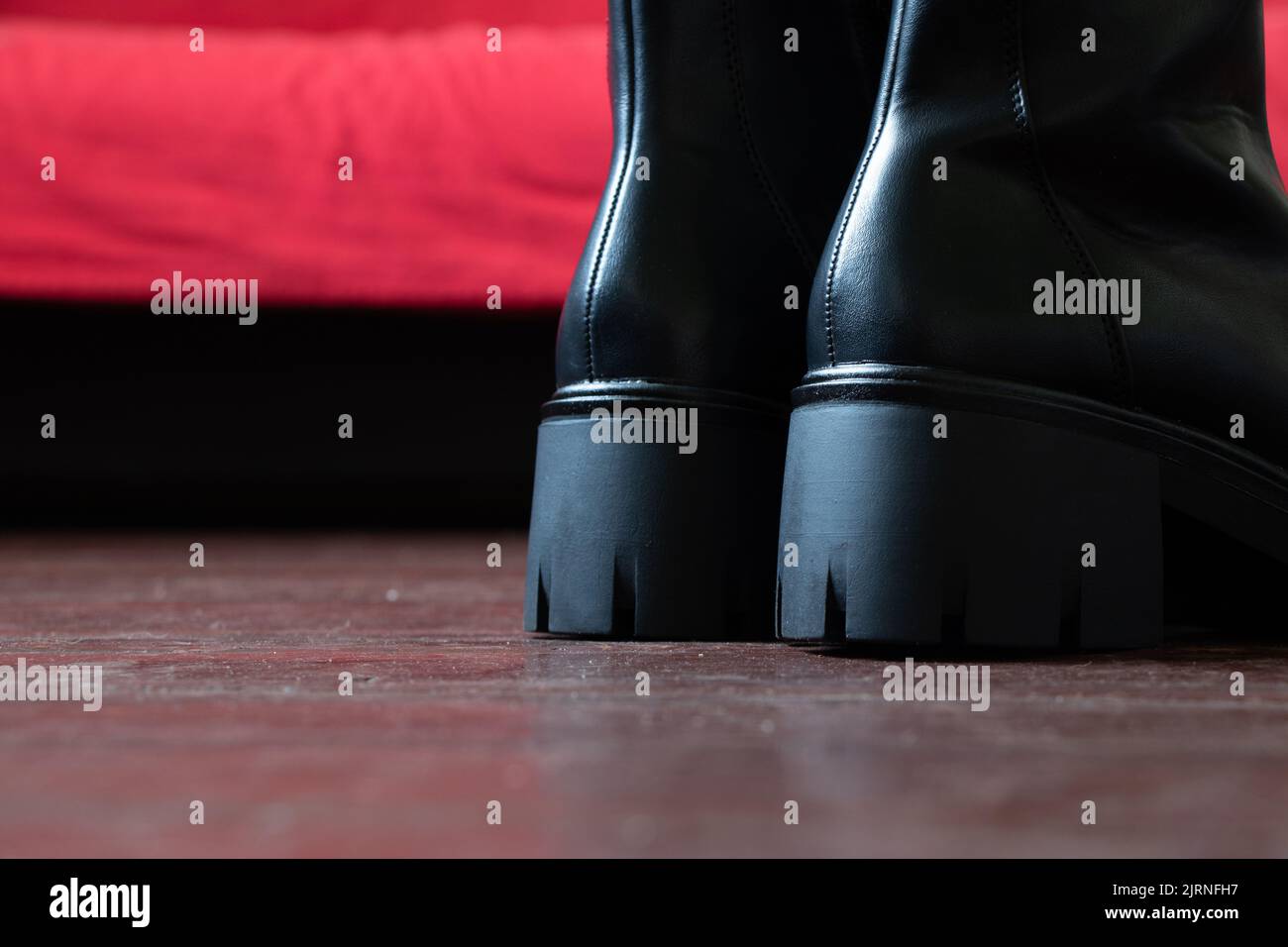 Mädchen in hohen schwarzen Stiefeln auf dem alten schmutzigen Boden zu Hause, Damenschuhe, Füße in Schuhen auf dem Boden, Schuhe auf dem Holzboden Stockfoto