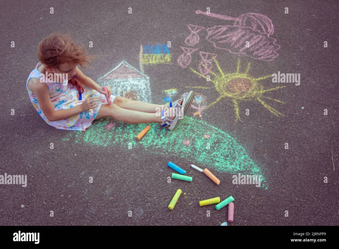 Das ukrainische Mädchen Kind zeichnet Kinderzeichnungen mit Kreide auf den Bürgersteig. Stockfoto