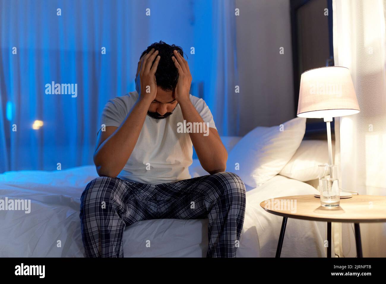 Gestresster indischer Mann, der nachts auf dem Bett saß Stockfoto