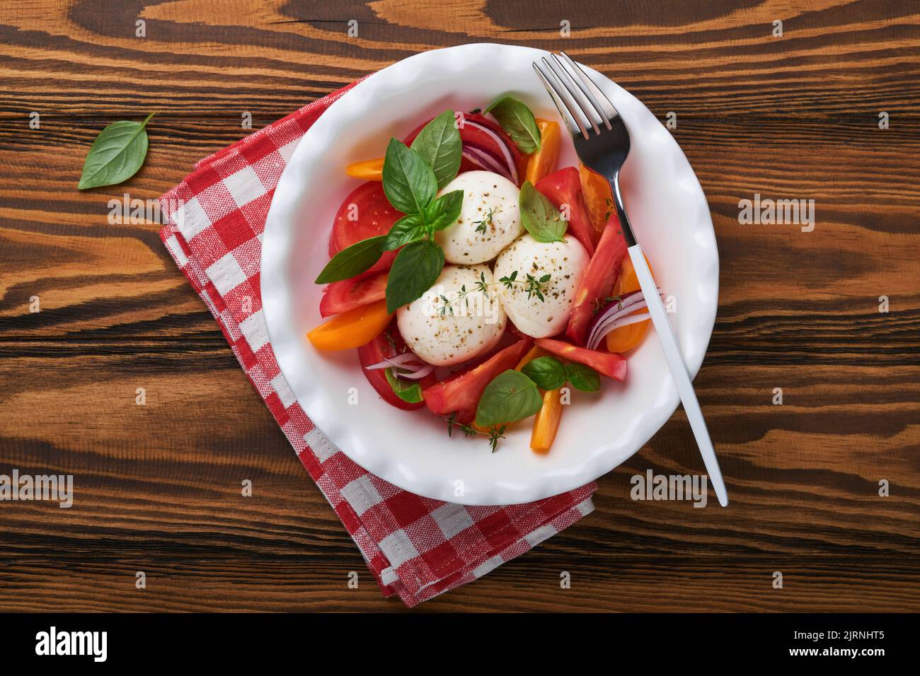 Caprese-Salat. Italienischer Caprese-Salat mit geschnittenen Tomaten, Mozzarella-Käse, Basilikum, Olivenöl auf weißem Teller auf altem braunem Holzhintergrund. Delikatesse Stockfoto