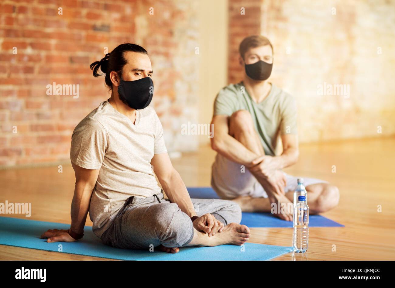 Männer in Masken ruhen sich im Yoga-Studio aus Stockfoto