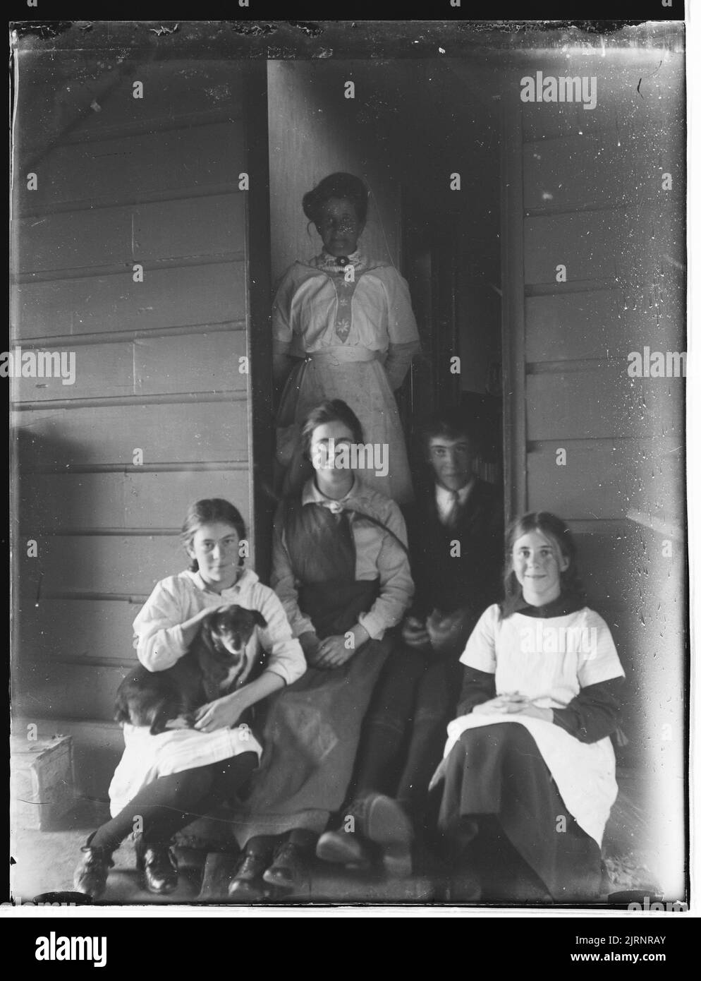 Gruppenportrait vor der Haustür - 2 Frauen, 1 Mann, 2 Mädchen und ein Hund, von Crombie und Permin. Stockfoto