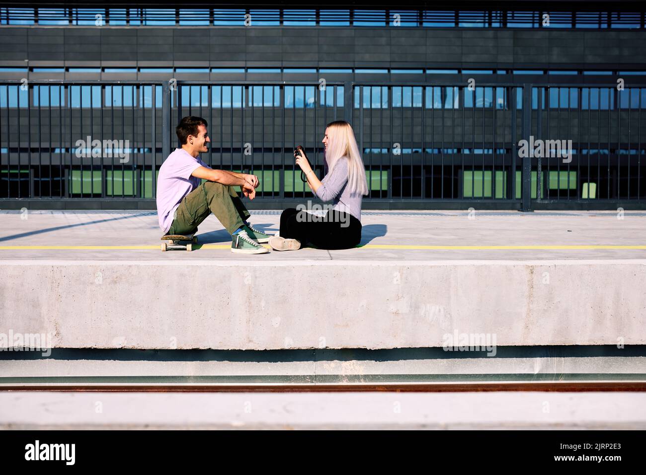 Ein glückliches Teenager-Paar sitzt am Bahnhof und macht Fotos. Stockfoto
