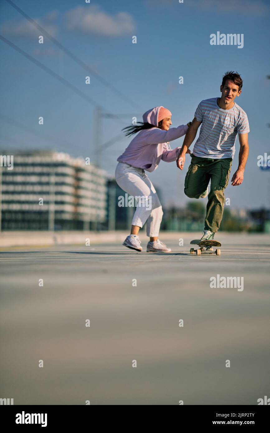 Spielerische Teenager spielen Spiele. Ein Junge, der auf einem Skateboard reitet, während ein Mädchen ihn schob. Stockfoto