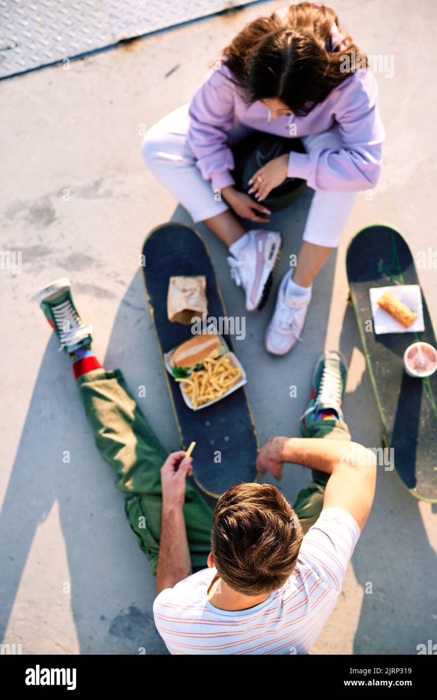 Draufsicht auf Jugendliche, die auf ihren Skateboards Fast Food essen. Selektiver Fokus auf den Kopf eines Teenagers, der mit seiner Freundin sitzt. Stockfoto