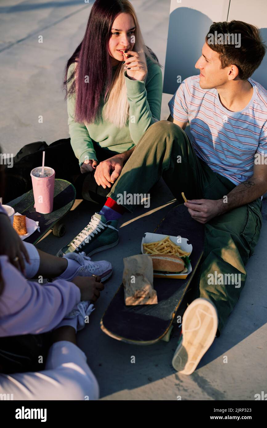 Eine kleine Gruppe von Teenagern, die draußen sitzen und Fast Food für einen Snack essen. Urbane Jugendliche hängen nach der Schule ab. Stockfoto