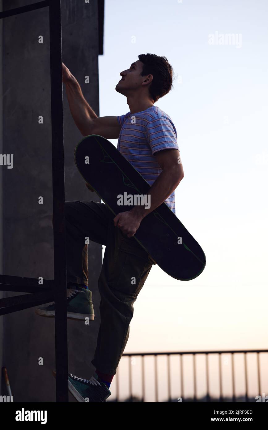 Die Silhouette eines rebellischen Teenagers klettert mit einem Skateboard in den Händen Leitern auf ein Gebäude. Stockfoto