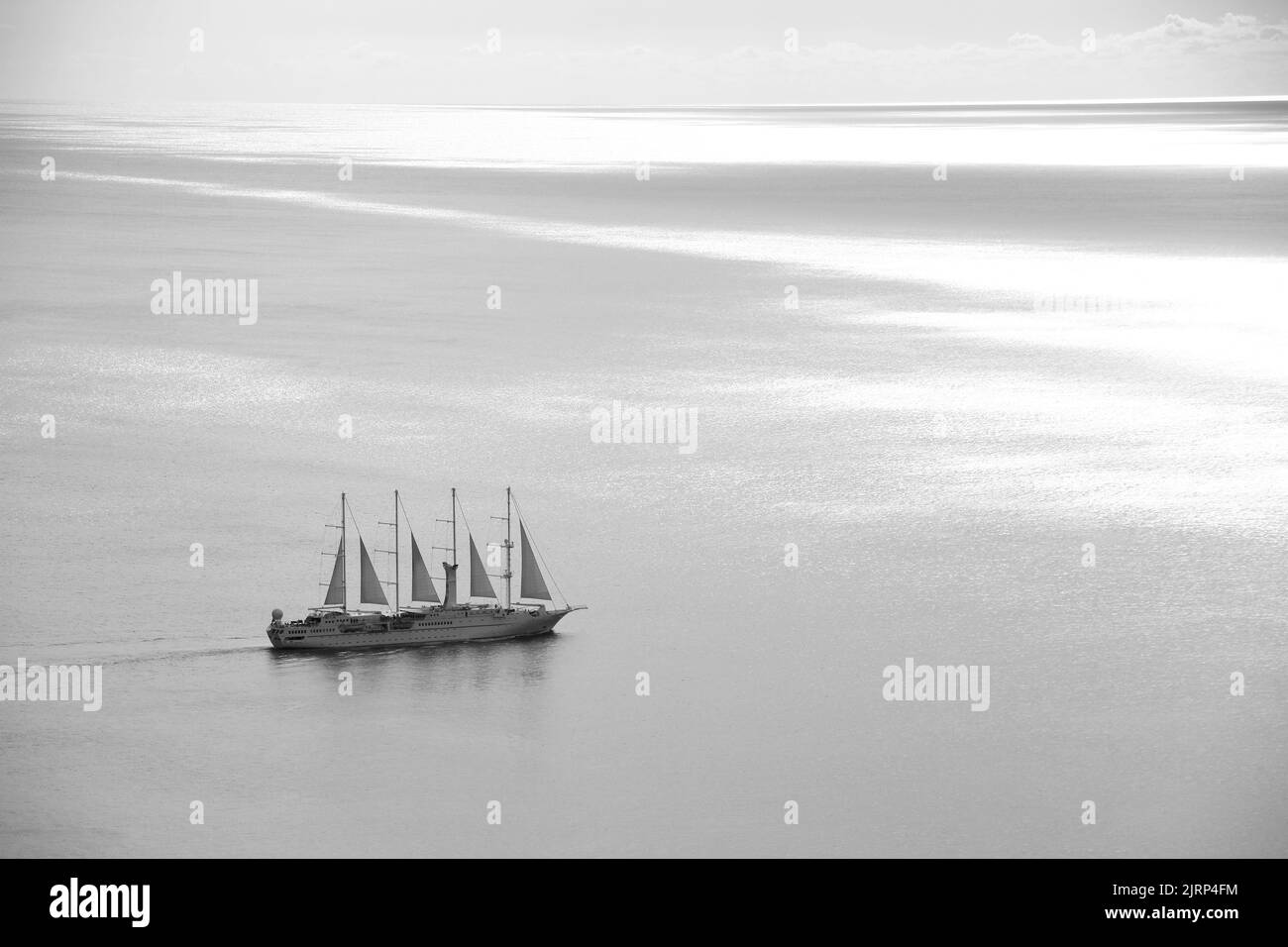 Schwarz-weißes Bild eines Segelbootes, das auf dem Meer segelt, mit dem Horizont im Hintergrund und dem Schatten der Wolken auf der Wasseroberfläche.sai Stockfoto